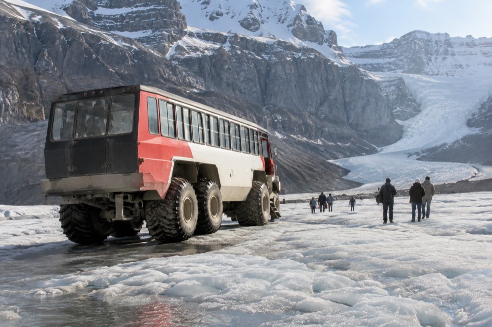 An all-terrain glacier vehicle parked on white ice with steep rock walls rising behind it