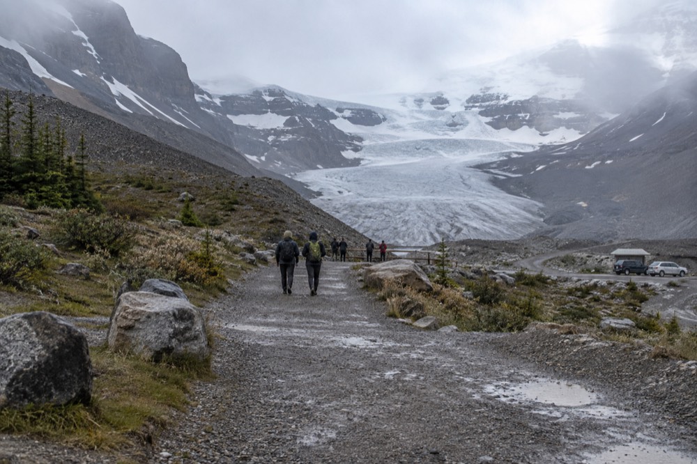 A maintained gravel trail leading toward the terminus of a glacier with a barrier fence at its end