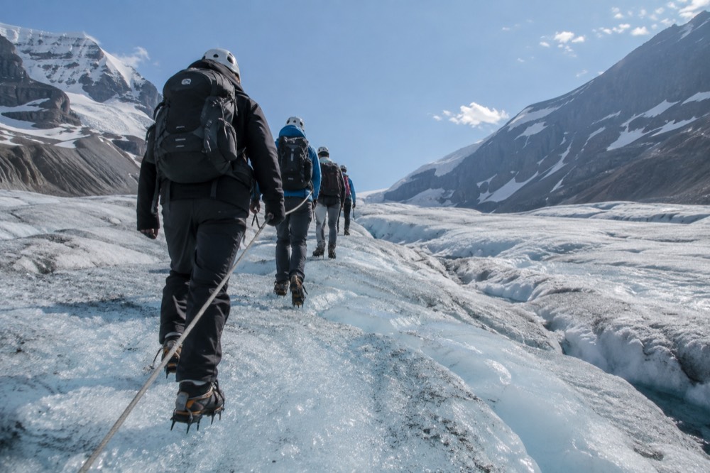 A guided hiking group in helmets and crampons walking in a line across a blue glacier surface