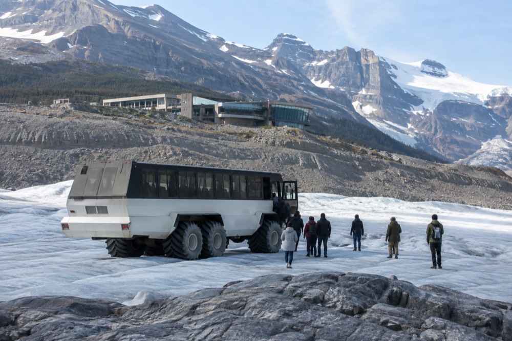 An all-terrain ice vehicle parked on a glacier with visitors standing on the ice nearby