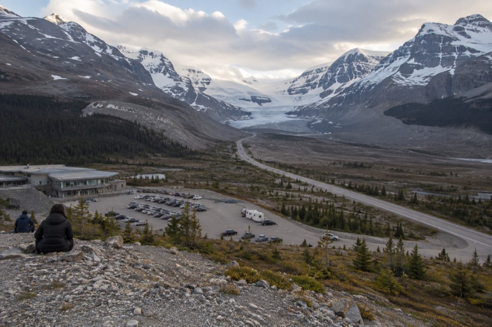 A mountain highway winding north through a wide glacial valley with distant snow peaks