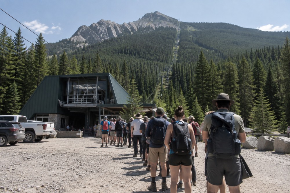 Long line of visitors waiting at a gondola base station under a blue sky