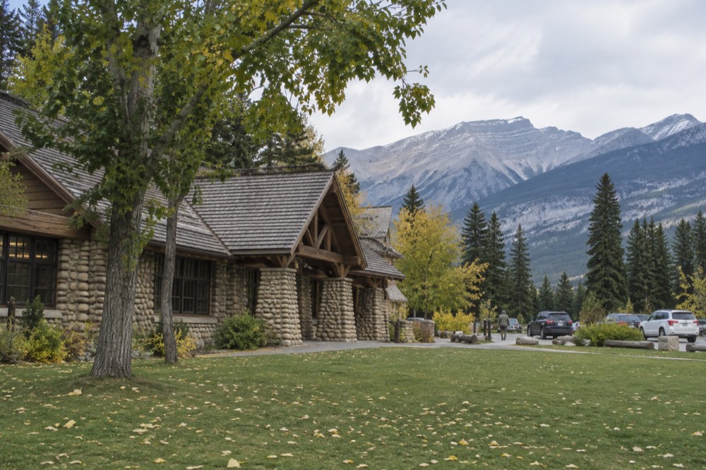A visitor information centre building in Jasper townsite with mountains behind it on a summer day