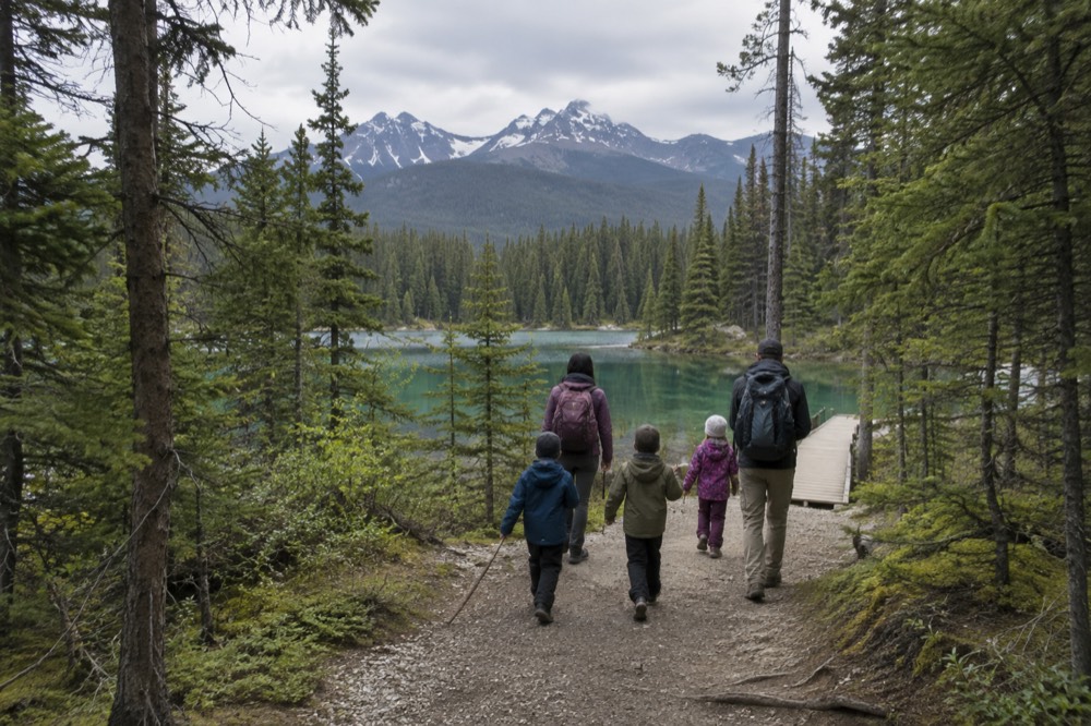 A family walking a forest trail toward a turquoise mountain lake in Jasper National Park