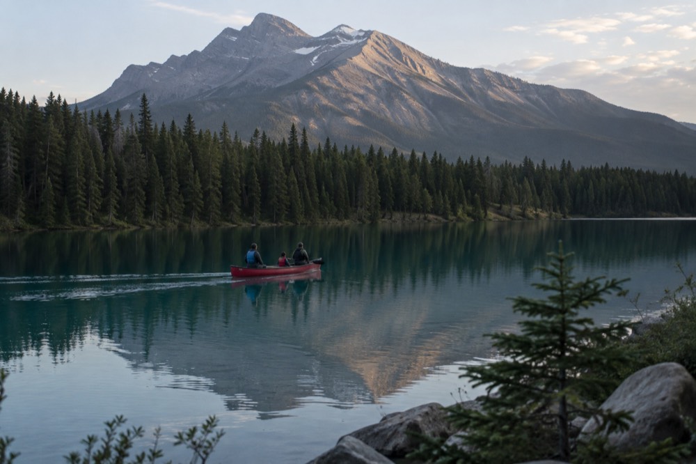 A guided canoe gliding across a calm mountain lake with forested peaks reflected in the water