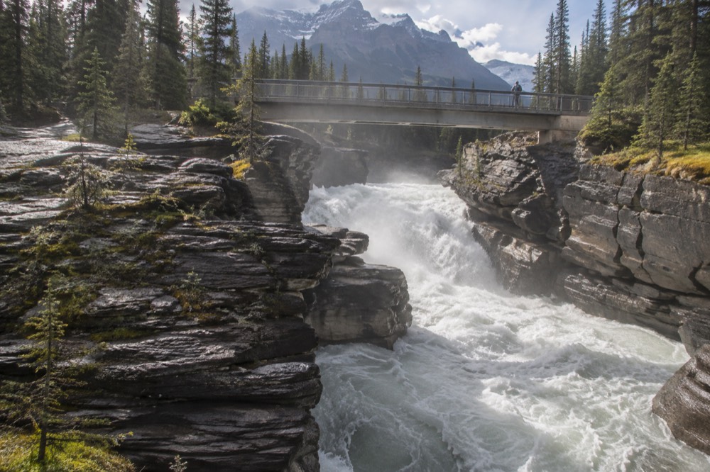 A waterfall pouring through a narrow rock gorge with a footbridge above it