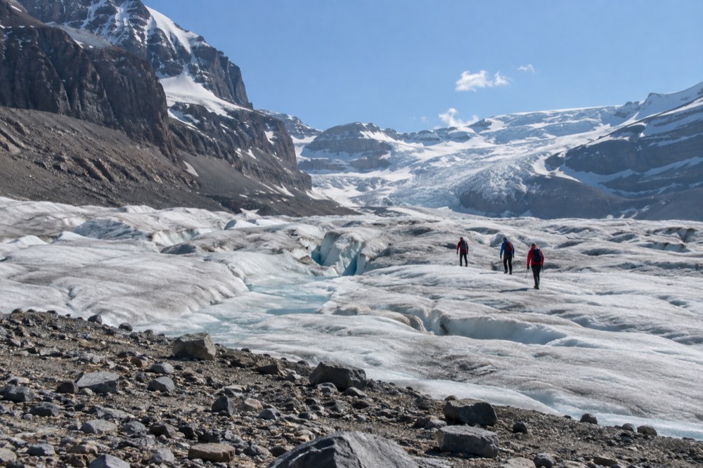 Hikers in warm jackets walking across a wide glacier tongue under bright sun