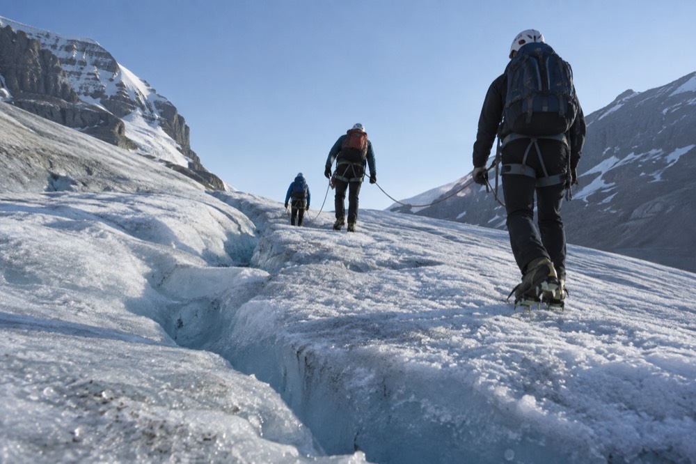 A small roped group of hikers crossing blue glacier ice with crampons