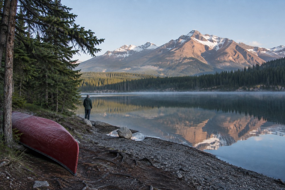 A calm lake reflecting snowy mountain peaks under a clear morning sky