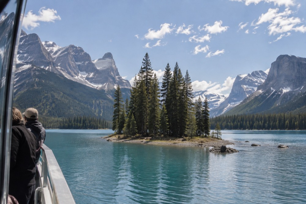 A small forested island in a blue mountain lake with peaks behind it