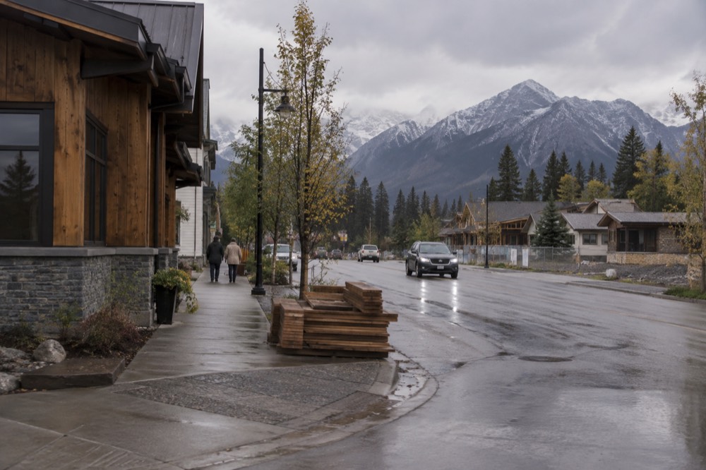 Downtown street in a mountain town with storefronts, sidewalks and peaks rising behind the rooftops