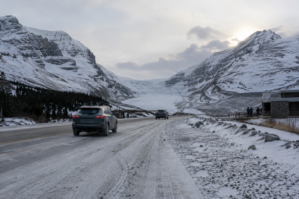 A snow-dusted mountain highway winding along a turquoise river between high peaks
