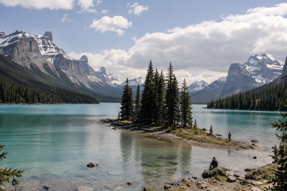 A small forested island with pines standing in turquoise lake water between mountain ridges