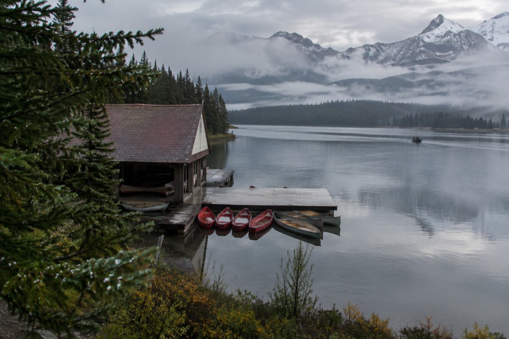 Morning mist over a long mountain lake with a wooden boathouse and small boats at a dock