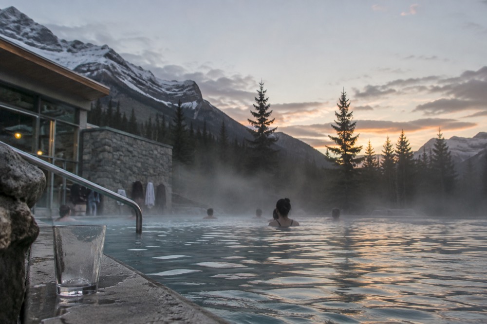 Steaming water surface of an outdoor pool with mist drifting across forested slopes at dusk