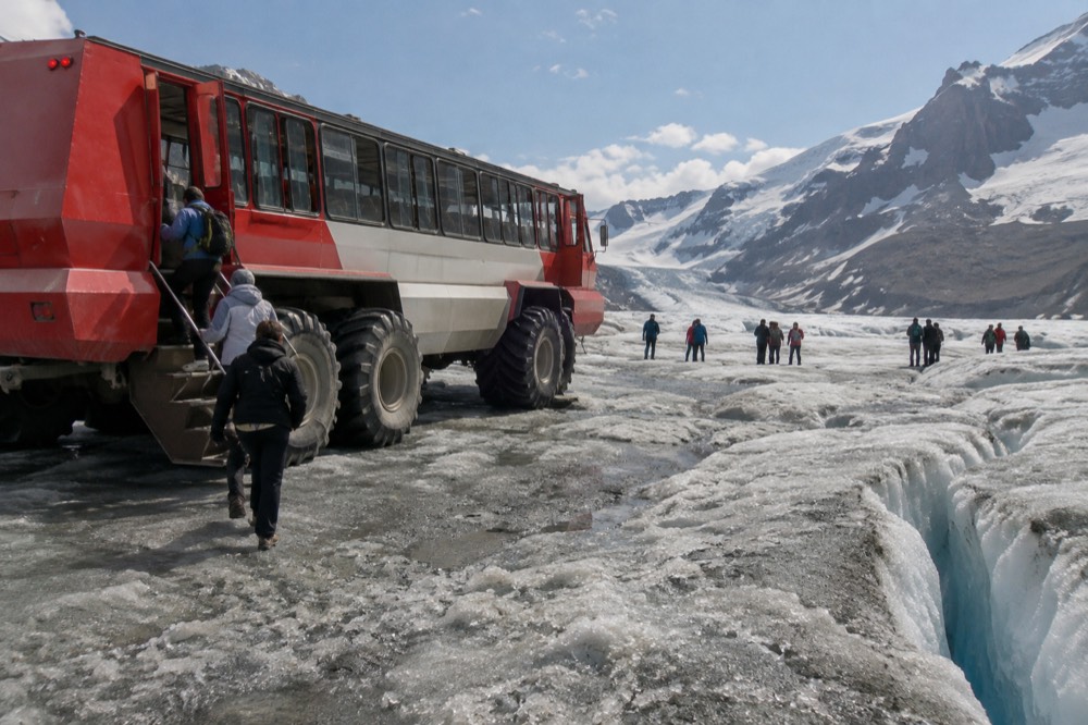 An Ice Explorer vehicle parked on the Athabasca Glacier with passengers stepping onto the ice