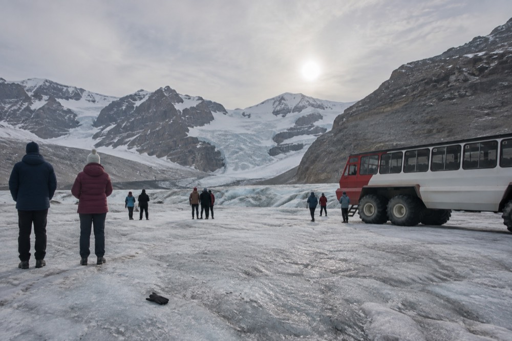 Visitors standing on the Athabasca Glacier in warm jackets near an Ice Explorer vehicle