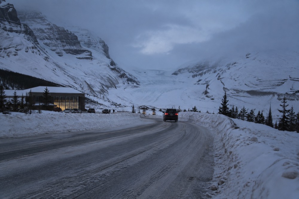 A snow-packed mountain highway with plowed edges and peaks under low winter light