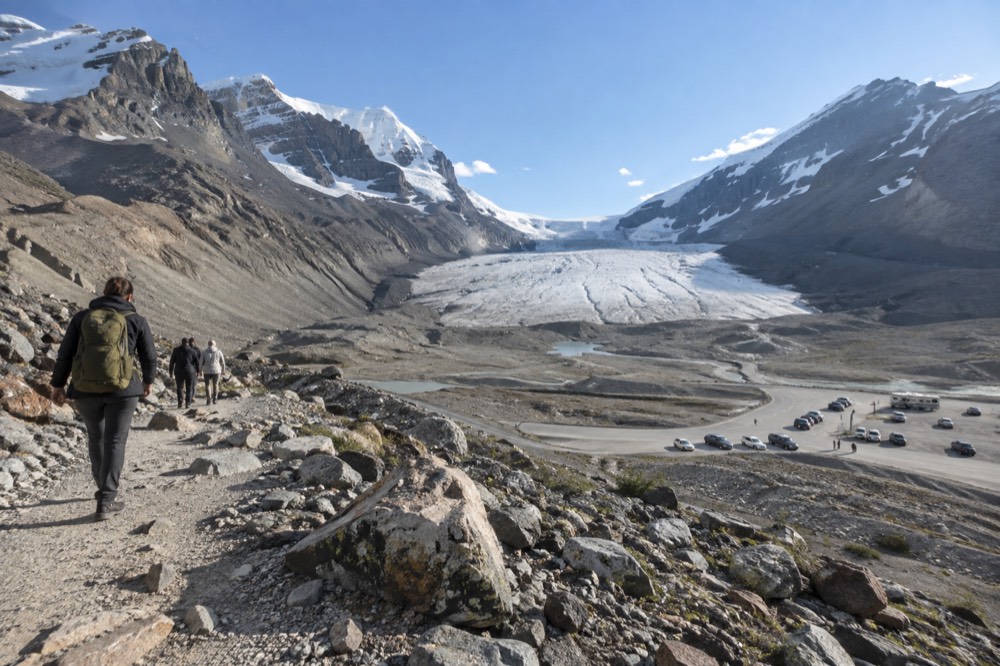 A steep mountain highway descending toward a glacier and a large icefield under clear sky