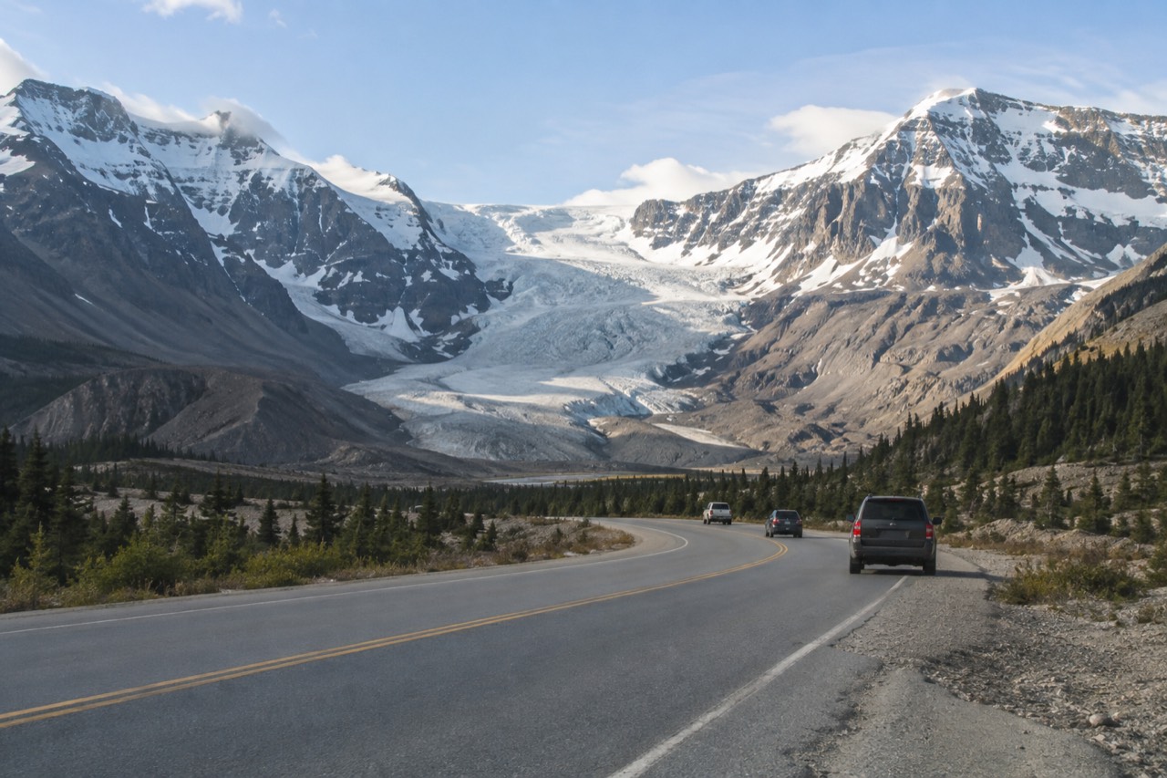 A quiet mountain highway winding between snow-covered peaks and a glacial river valley