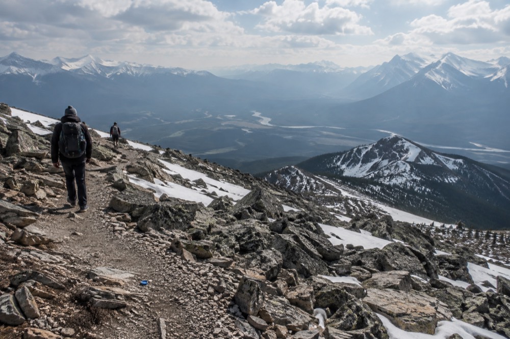 Rocky summit ridge above the treeline with a winding trail and wide valley views under scattered clouds
