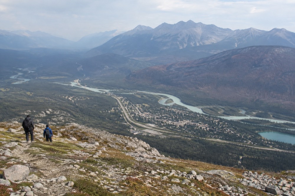View from a mountain ridge over a small townsite beside a river winding through a wide forested valley