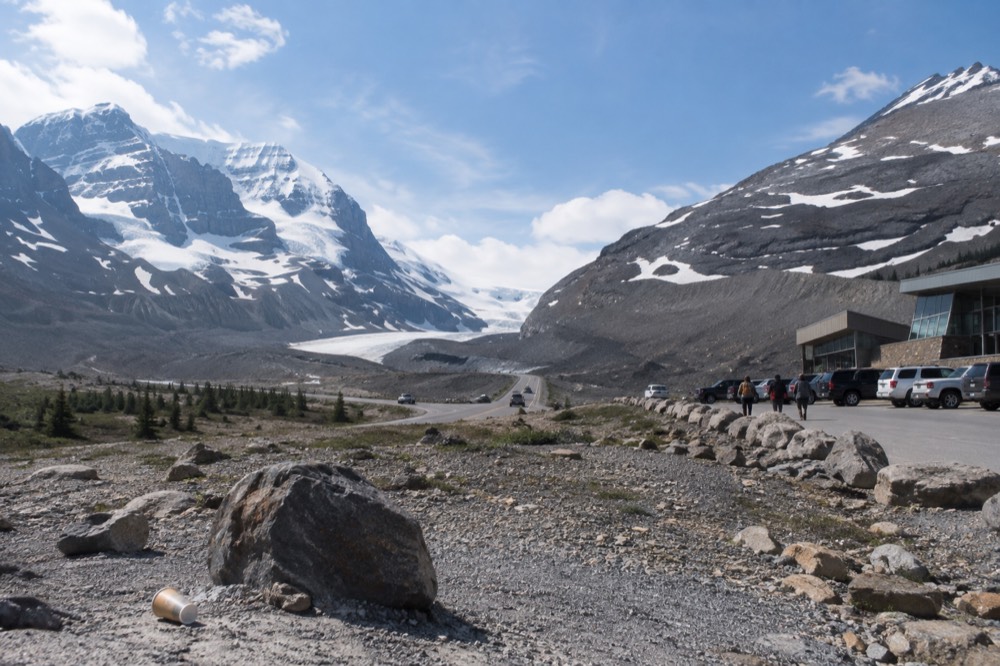 A road curving toward tall snow-covered mountains under a clear blue sky