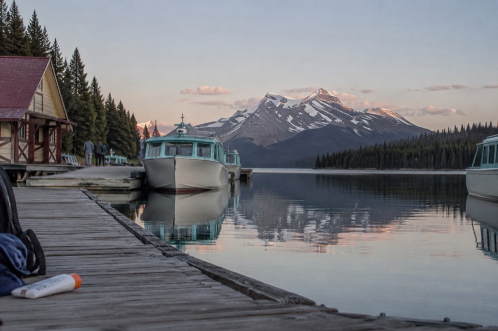 Wooden cruise dock on Maligne Lake with moored boats and mountains reflected in still water