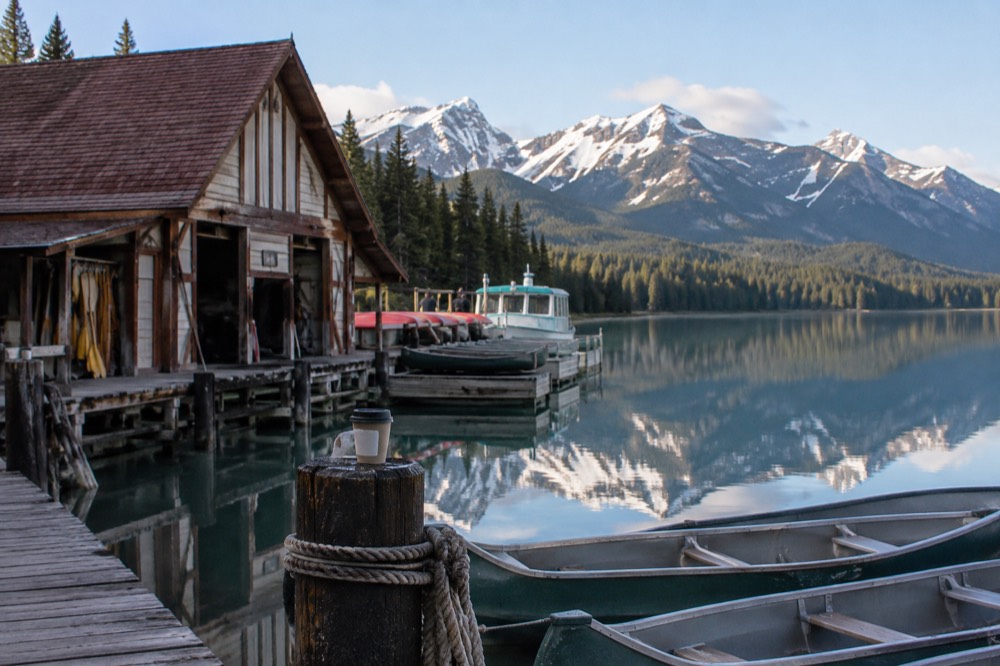 Morning light on Maligne Lake with calm water and mountains reflected near the boathouse
