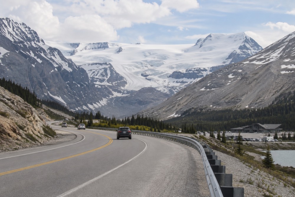 A winding mountain road crossing a pass with a vast icefield visible on the horizon