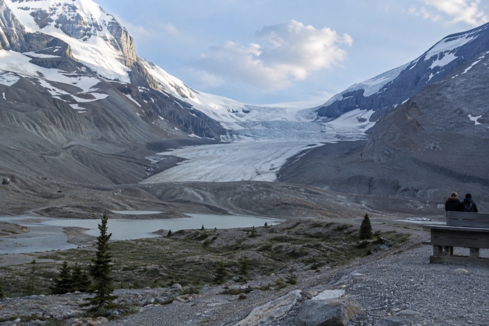 A glacier tongue flowing down between dark rock ridges toward a valley road