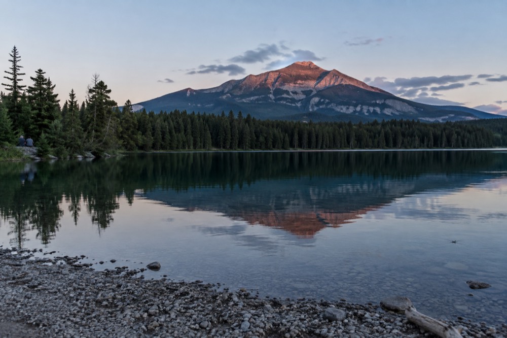 A calm mountain lake reflecting pine forest and distant peaks