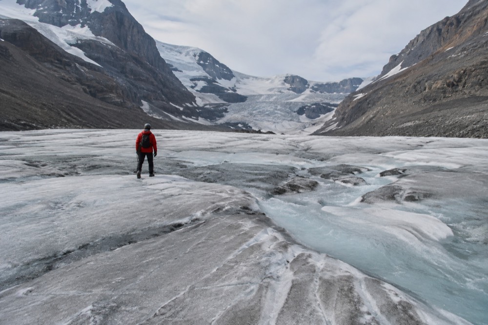 A person in a red jacket and helmet standing on a wide expanse of glacier ice