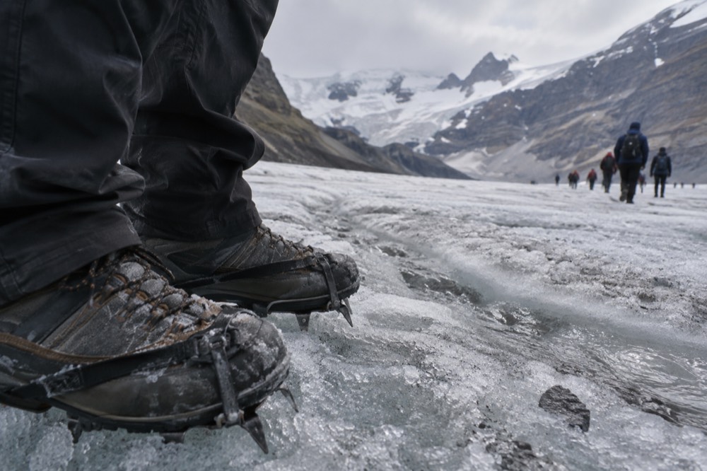 Hiking boots with steel crampons strapped on, resting on grey glacier ice