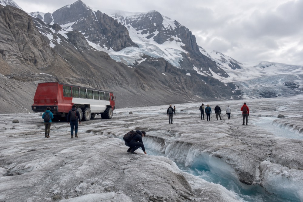A large all-terrain vehicle on a glacier with passengers standing on the ice