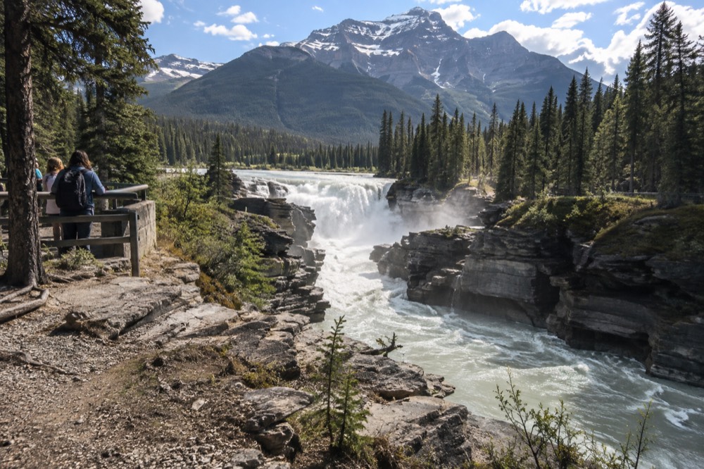 A turquoise river running through a wide mountain valley with a waterfall in the distance