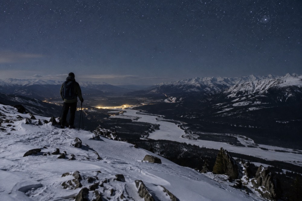 Snow covered valley with frozen river and mountains under a starry sky