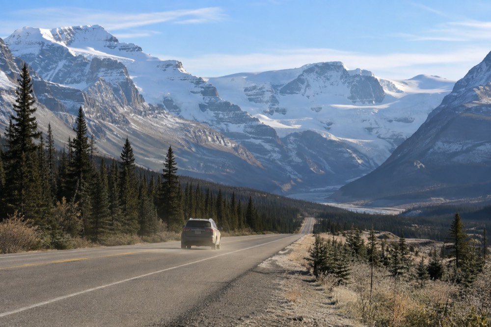 A mountain highway running down a long valley toward a wide wall of ice at the head of the valley