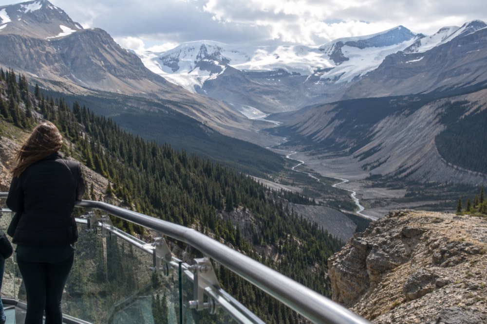 A visitor viewpoint with a railing looking out over a deep u-shaped valley carved by a glacier, with layered rock walls on both sides