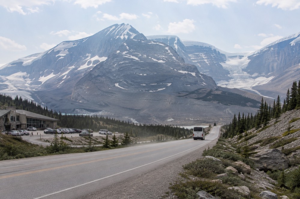A long straight mountain road leading toward a distant icefield with a tour bus travelling along it