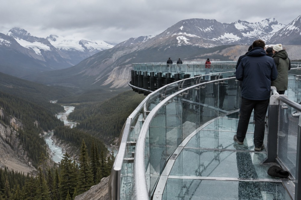 A glass-floored walkway curving along a cliff edge above a deep forested river valley
