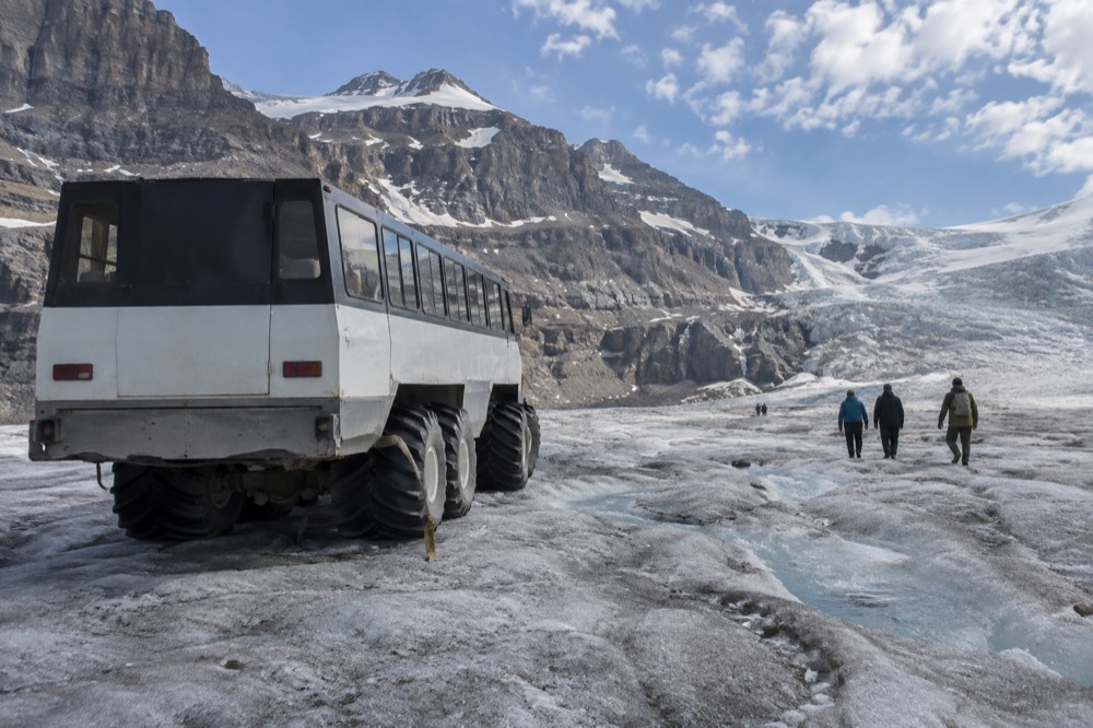 A large all-terrain vehicle with oversized tires parked on a snow-covered glacier with visitors boarding