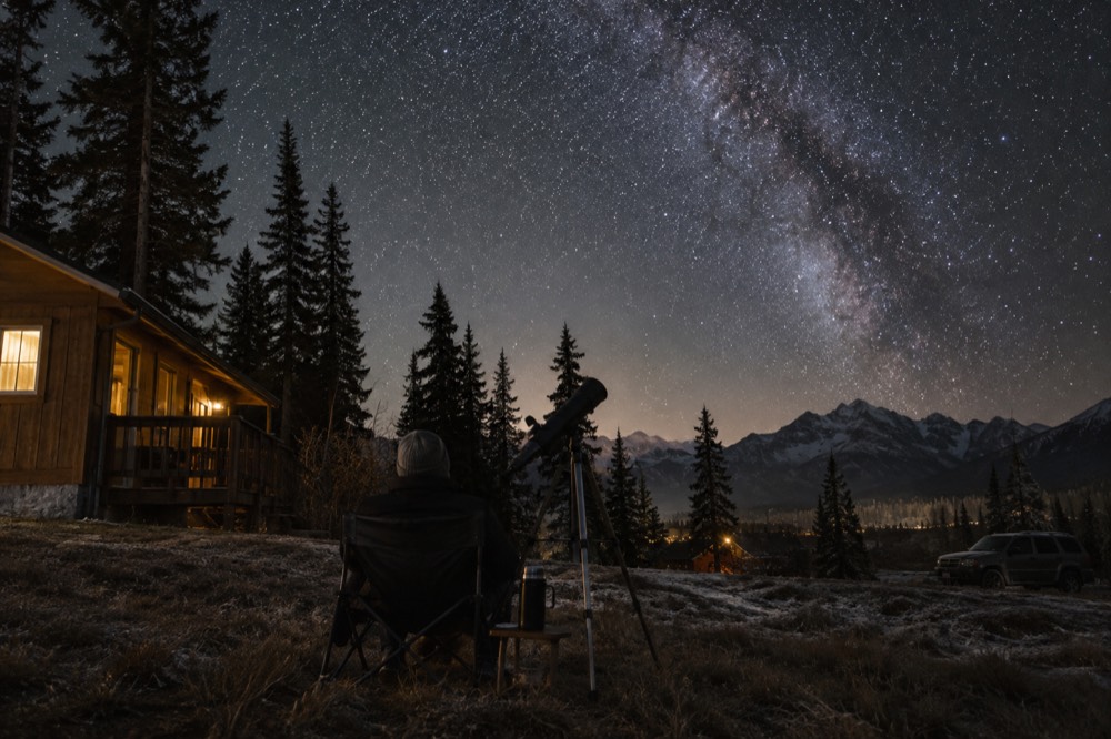 A telescope silhouetted against a starry sky beside a small building
