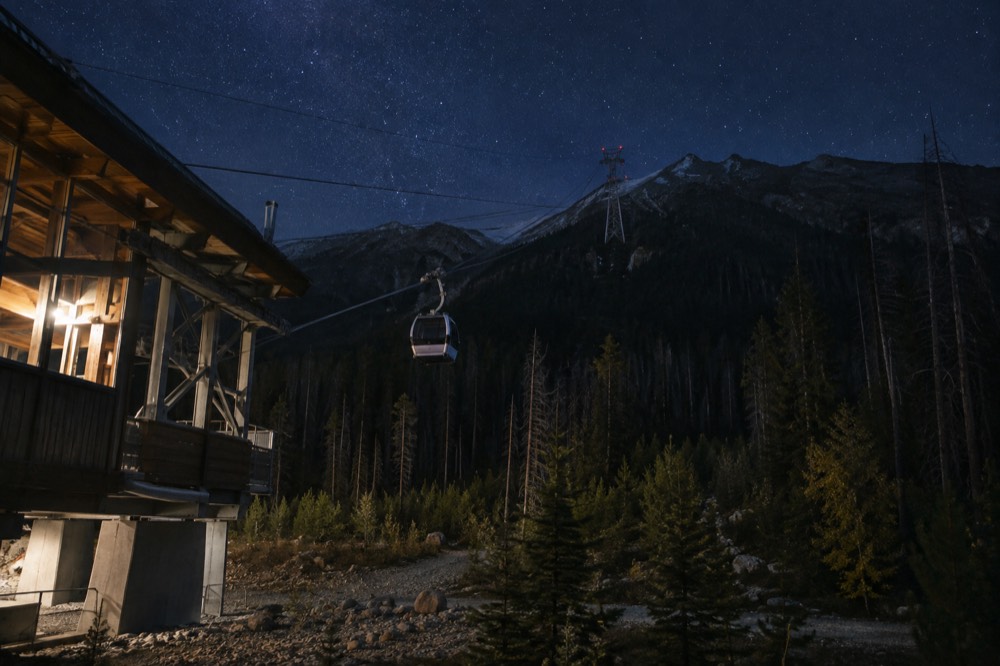 A gondola cabin on a cableway above dark forest under a starry sky