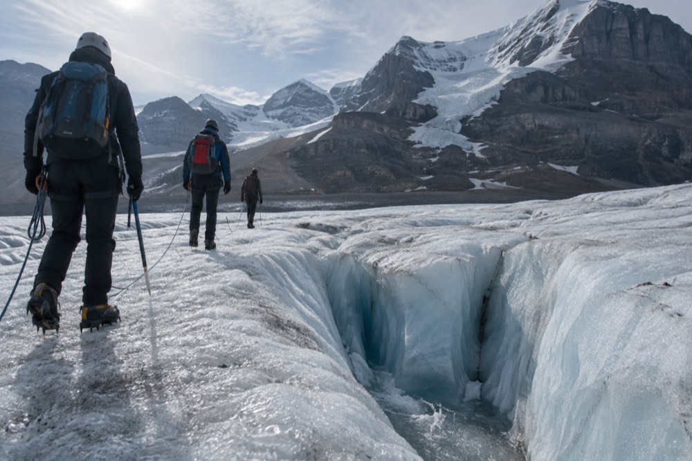 Hikers in crampons crossing blue glacier ice beside a deep crevasse