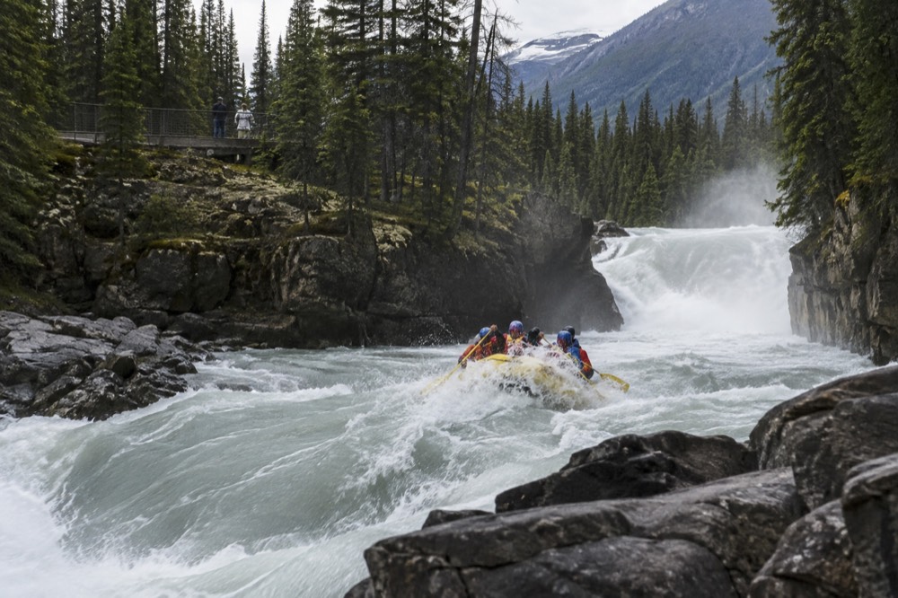 A guide raft passing through a wave train on a fast mountain river with mist rising