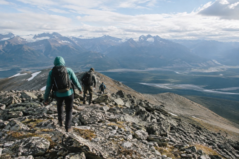Hikers on a rocky summit ridge above the tree line with wide valley and mountain panorama