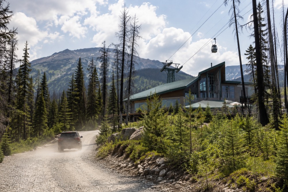 Mountain access road curving through evergreen forest toward a tramway base station building