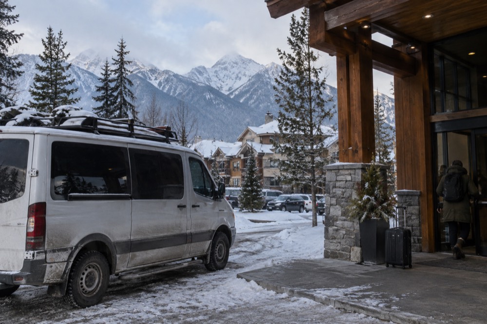 A guide van parked at a hotel entrance in Jasper with mountains behind the rooftops