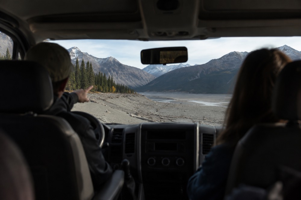 A tour guide pointing at mountain scenery while passengers look out from a vehicle